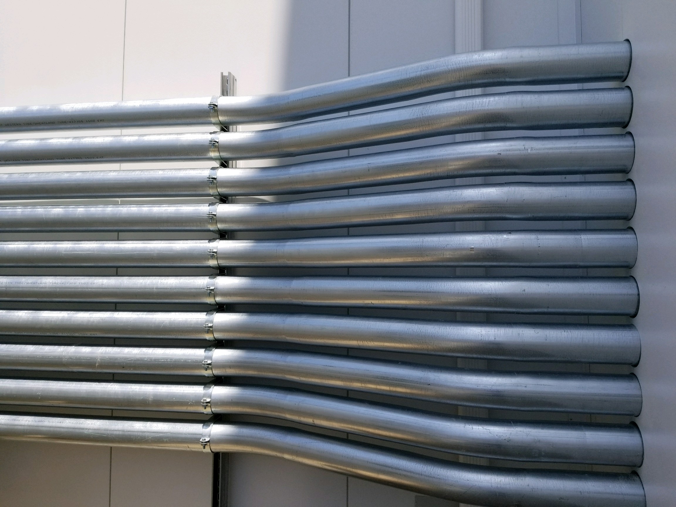 Row of precisely bent metal electrical conduit installed along an exterior wall, showcasing prefab tool accuracy and consistency.