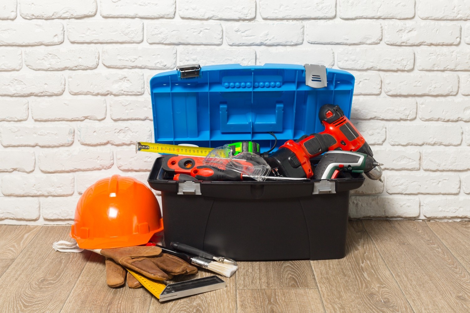 Open toolbox with power tools, gloves, and safety gear organized on wooden floor – professional tool storage solution.