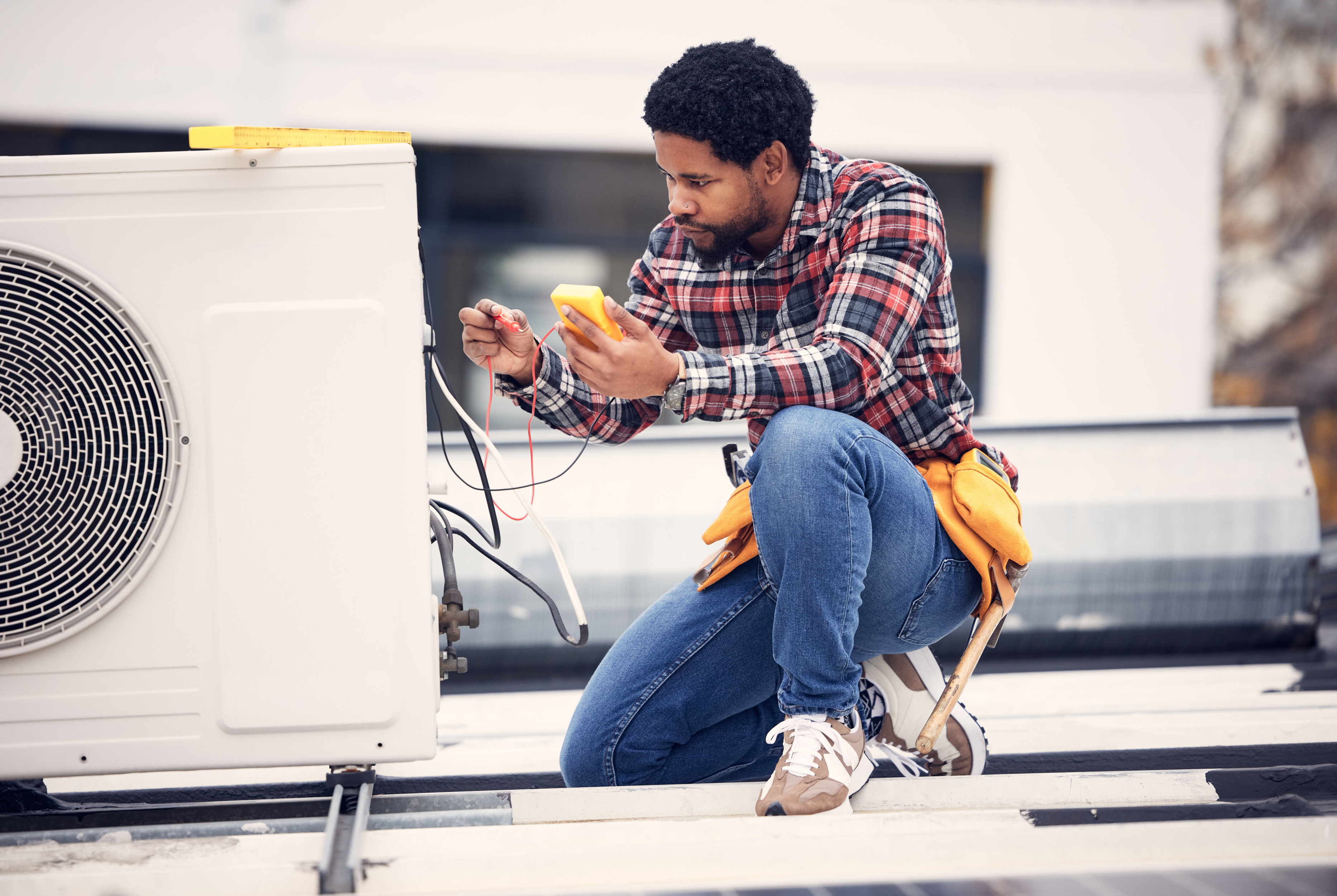 HVAC technician testing rooftop air conditioning unit installation with multimeter – secure mounting and electrical setup.