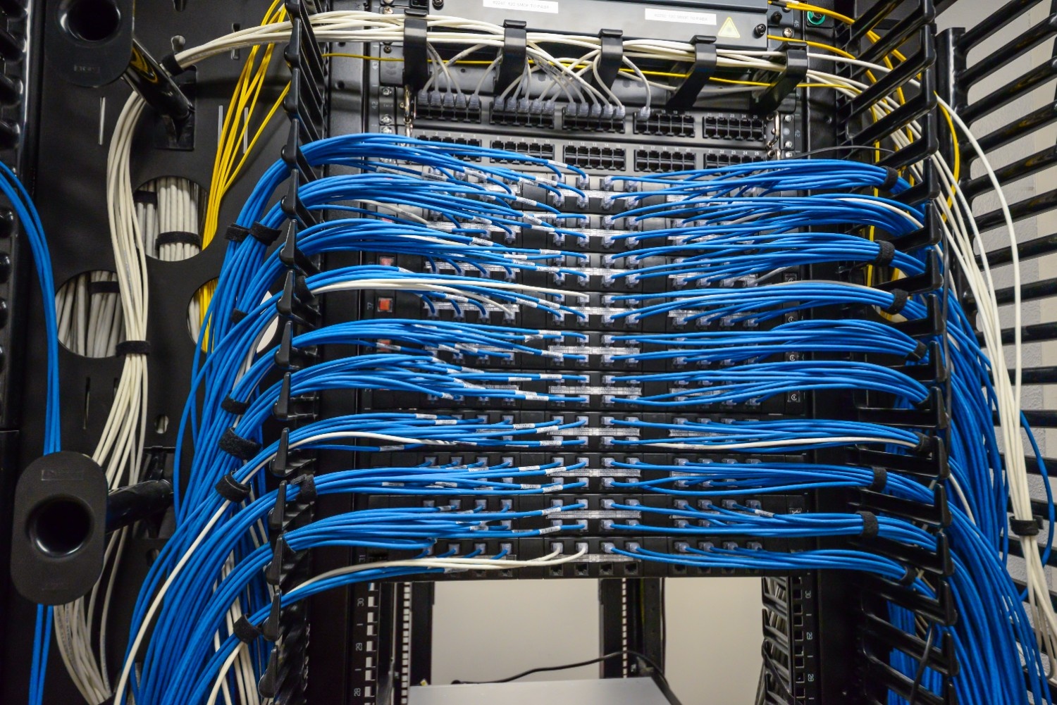 Structured cabling system with bundled blue Ethernet cables connected to network patch panels and switches in a server rack.