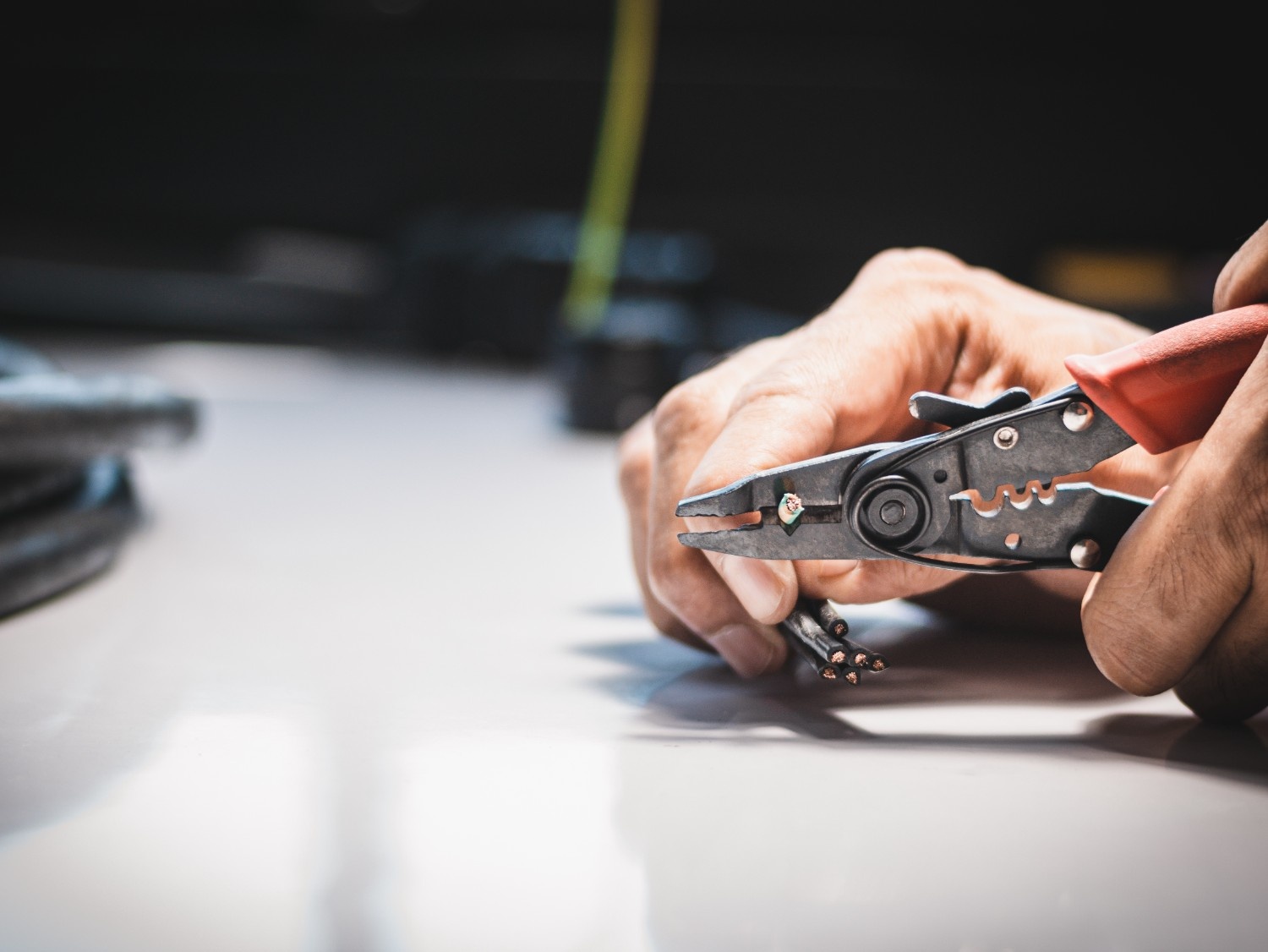 Electrician using a wire crimper and stripper tool to prepare electrical wire for installation or connection.