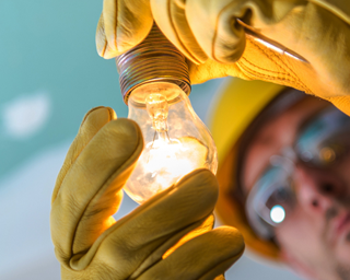 Electrician holding hard hat and gloves with tool belt—ready for on-site electrical work and safety compliance.