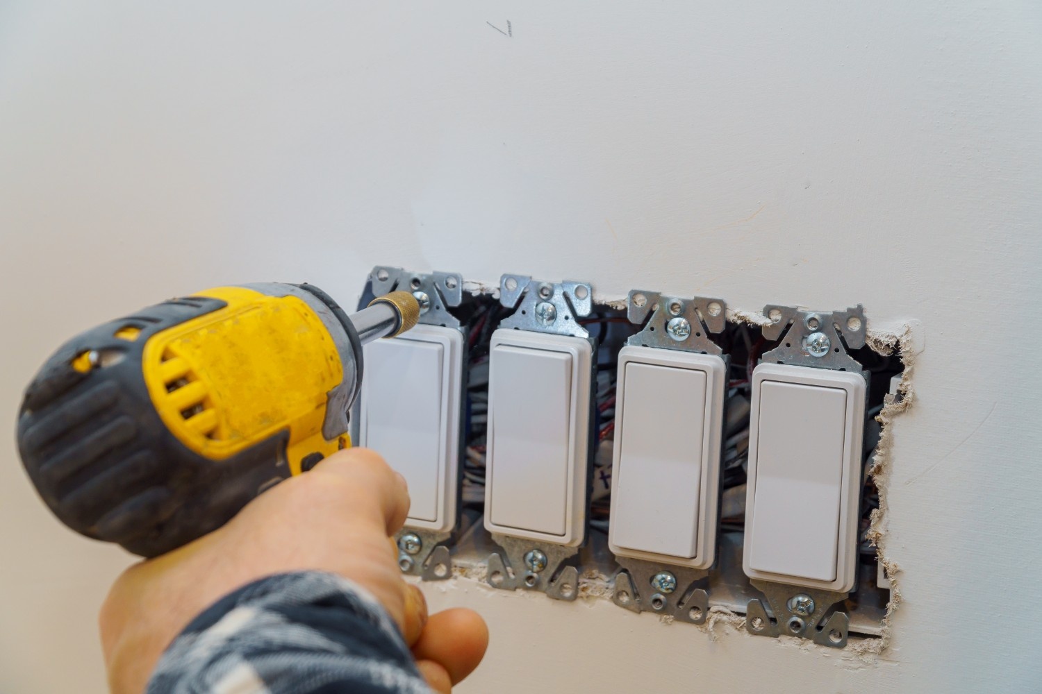 Electrician using cordless power drill to install light switches in drywall – reliable tool for uninterrupted electrical work.