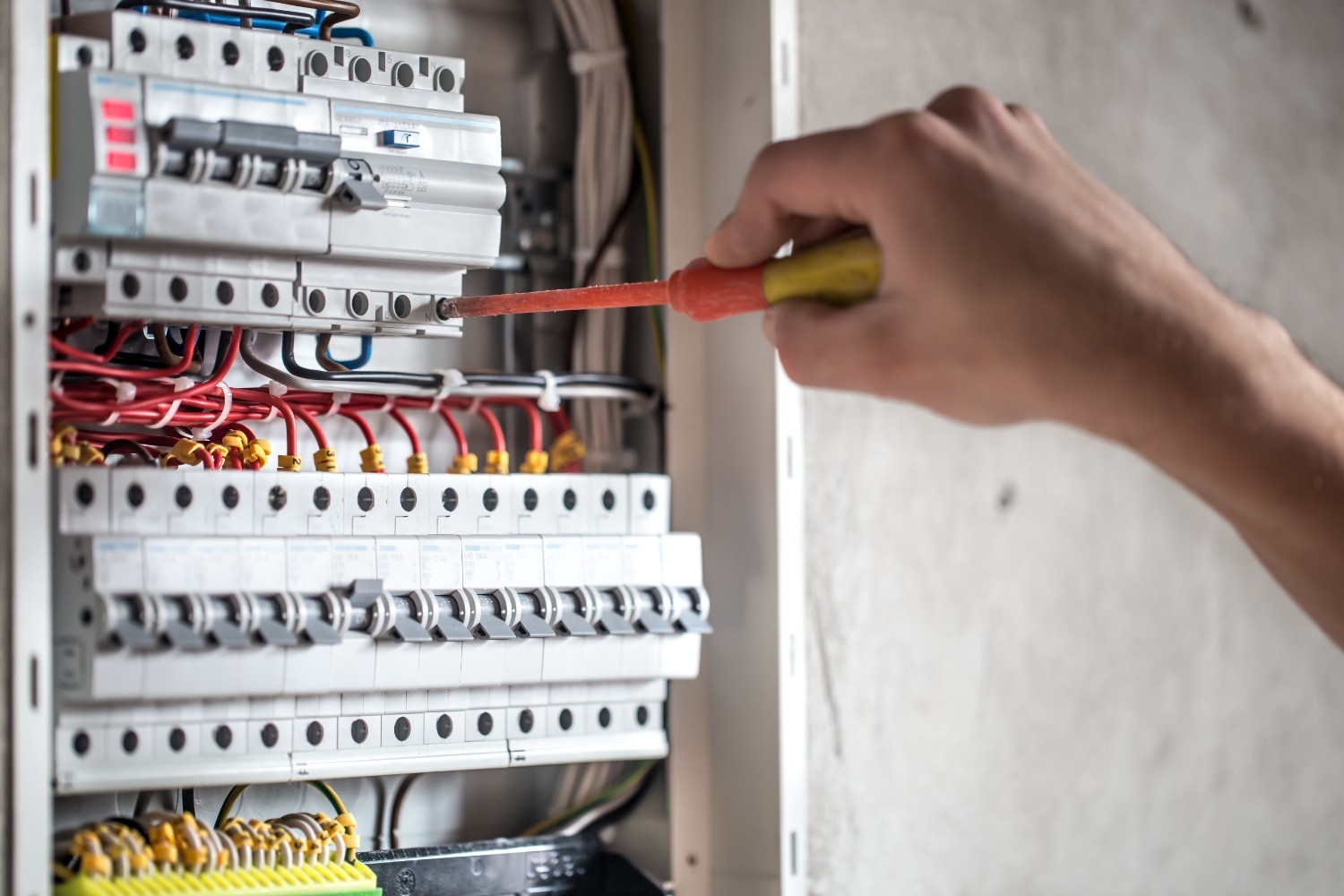 Close-up of electrician’s hand using insulated screwdriver on circuit breaker panel – professional electrical tool in action.